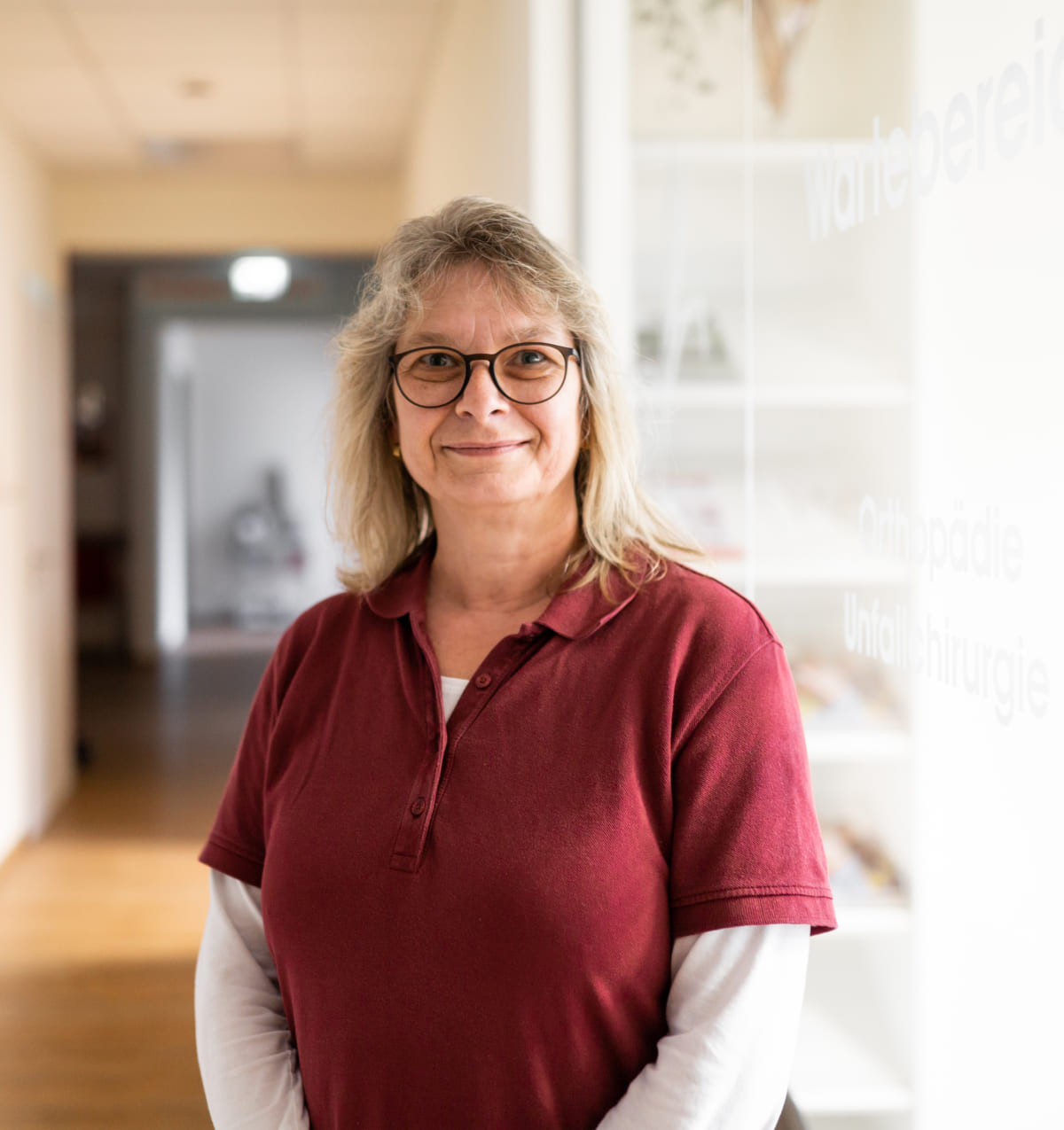 Eine Frau mit Brille steht selbstbewusst im Flur, nachdenklich und souverän.